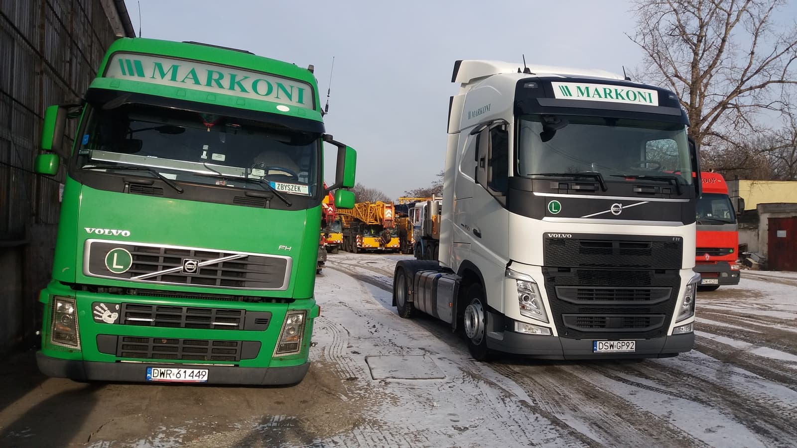 Dwa ciągniki Volvo z napisem MARKONI na placu zimą: zielony i biały